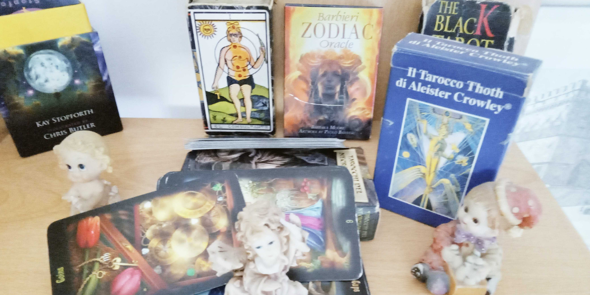 On the table are tarot cards, figurines of angels and closed packages with tarot cards.